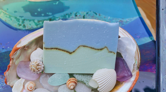 Bar of blue and green soap on a decorative plate with seashells and stones.