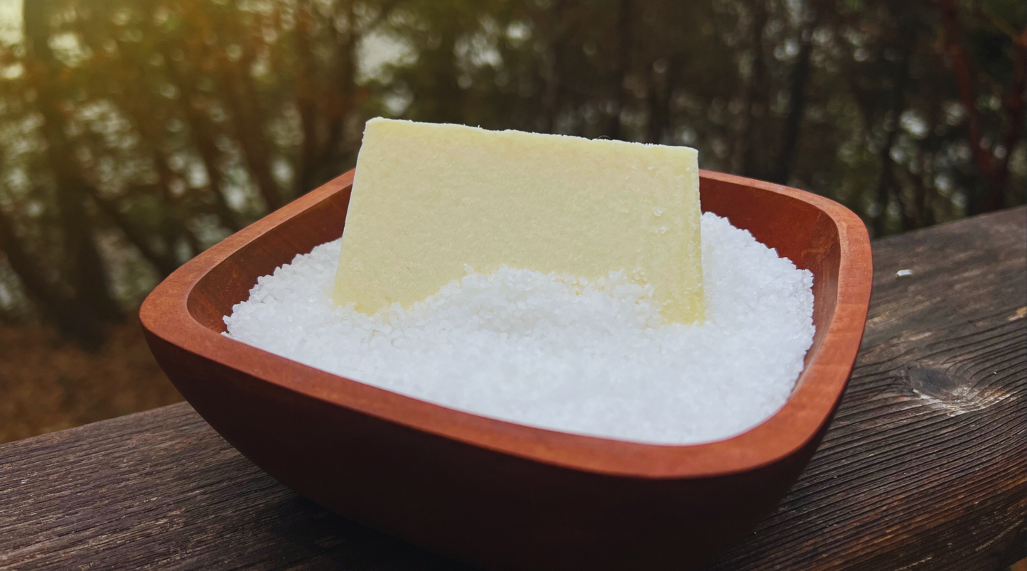 Bar of soap in a bowl of salt on a wooden surface with a blurred natural background