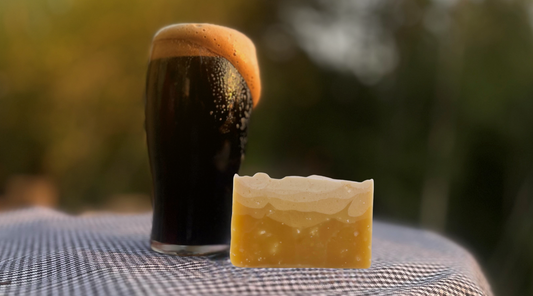 Dark beer with a thick head next to a bar of soap on a checkered surface outdoors.