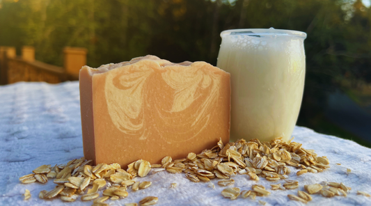 Bar of orange marbled soap, jar of milk, and oats on a textured surface with a blurred natural background