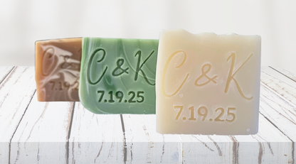 Three wedding bars of soap with 'C & K' and a date embossed on them, placed on a wooden surface.